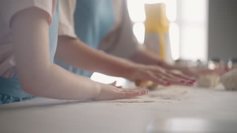 cooking-food-at-home-little-girl-and-woman-are-rolling-out-dough-on-kitchen-table-closeup-view